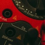 Czerwony multimetr z widoczną tarczą pomiarową i złączami