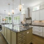 Jasna kuchnia z białymi szafkami i wyspą pod zlew z oświetleniem wiszącym