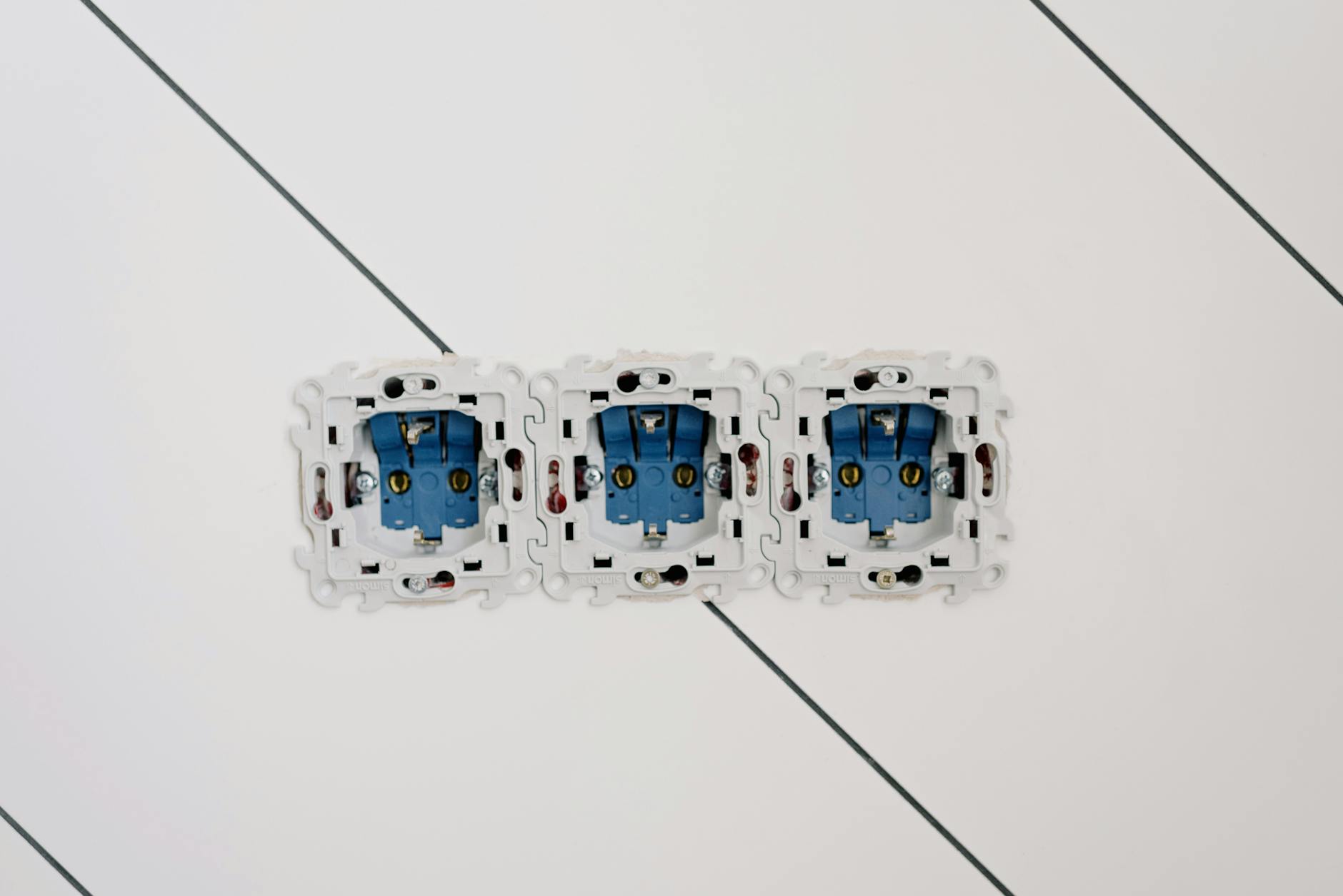 Zbliżenie na trzy niebieskie gniazdka elektryczne w białej ścianie