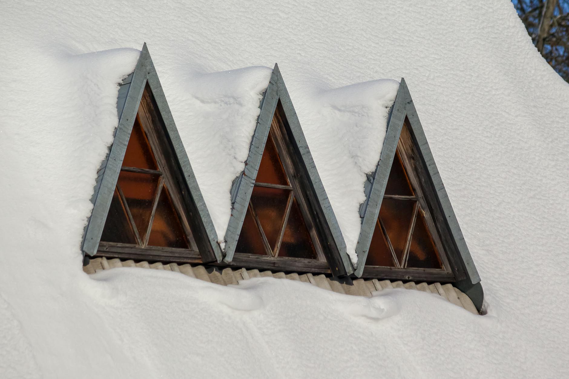 Zaśnieżony dach domu z trzema trójkątnymi oknami dachowymi