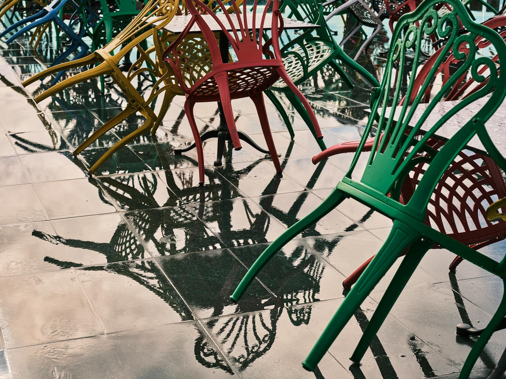 Metalowe krzesła odbijające się w mokrych płytkach na tarasie