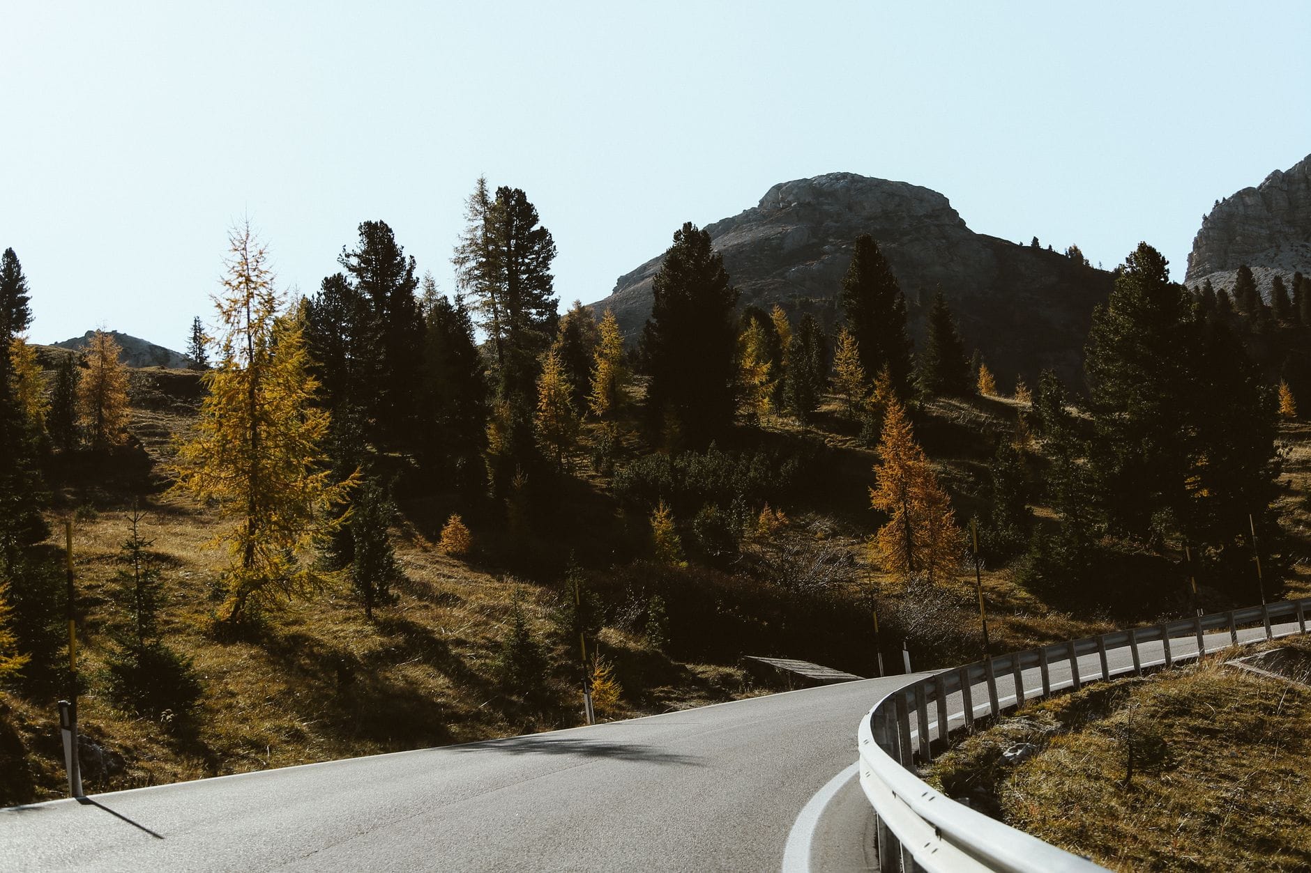 Kręta droga w Dolomitach otoczona jesiennymi drzewami i górskimi szczytami