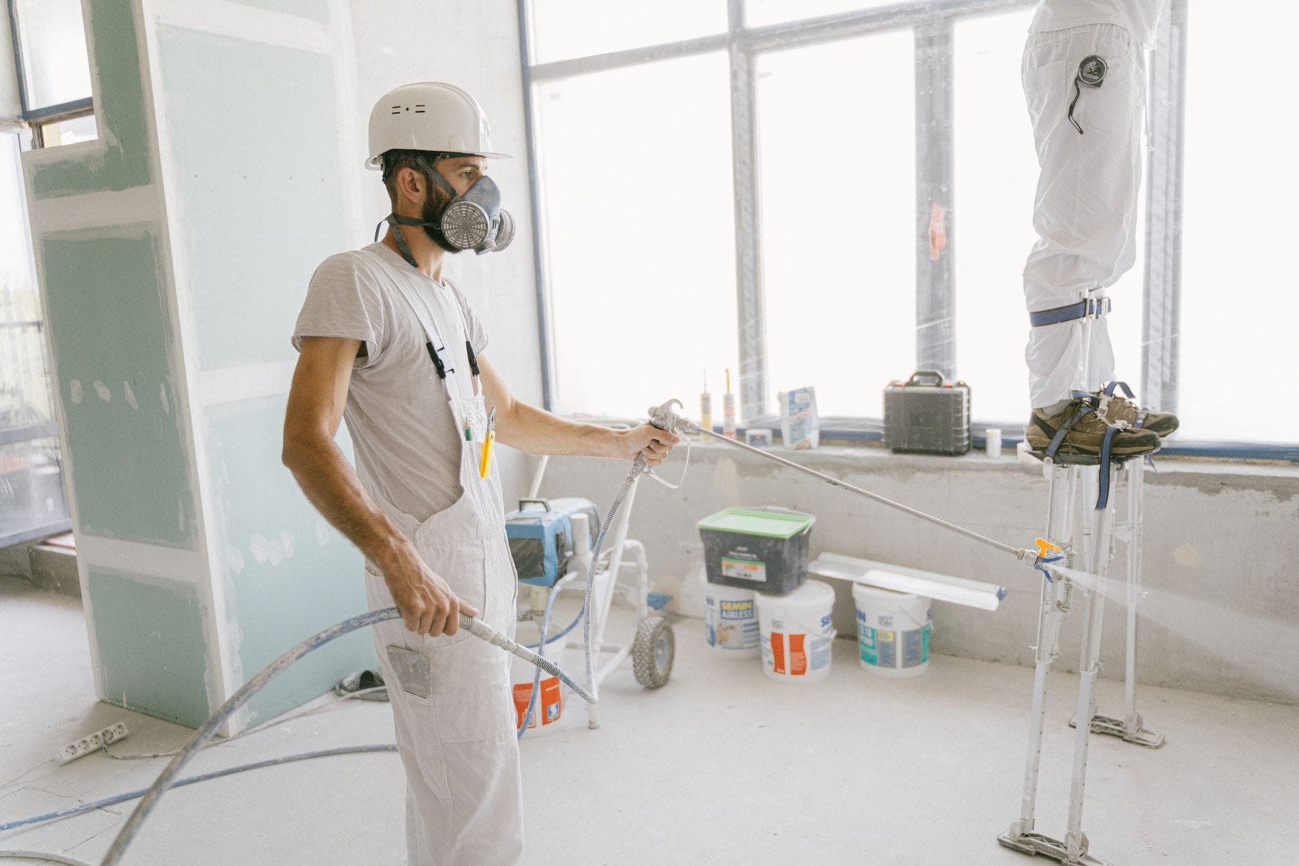 Dwaj pracownicy w kaskach malują ścianę wewnątrz ocieplanego domu